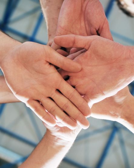 Übereinandergelegte Hände bilden ein Team: Unterstützung im Studium durch Coaching.